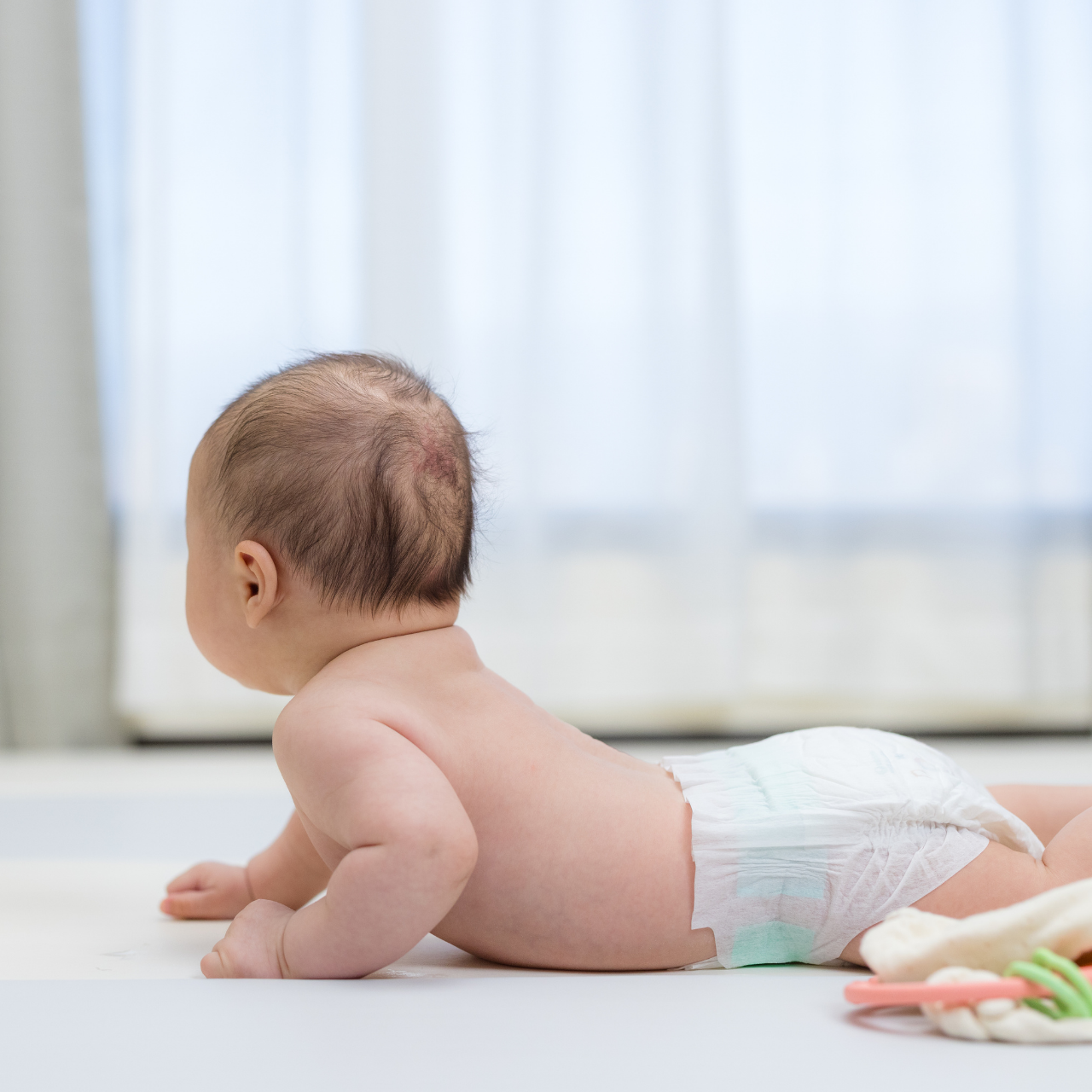Bebê de bruços apoiado nas mãozinhas, prestes a engatinhar, ilustrando marco de desenvolvimento motor dos 6 aos 12 meses