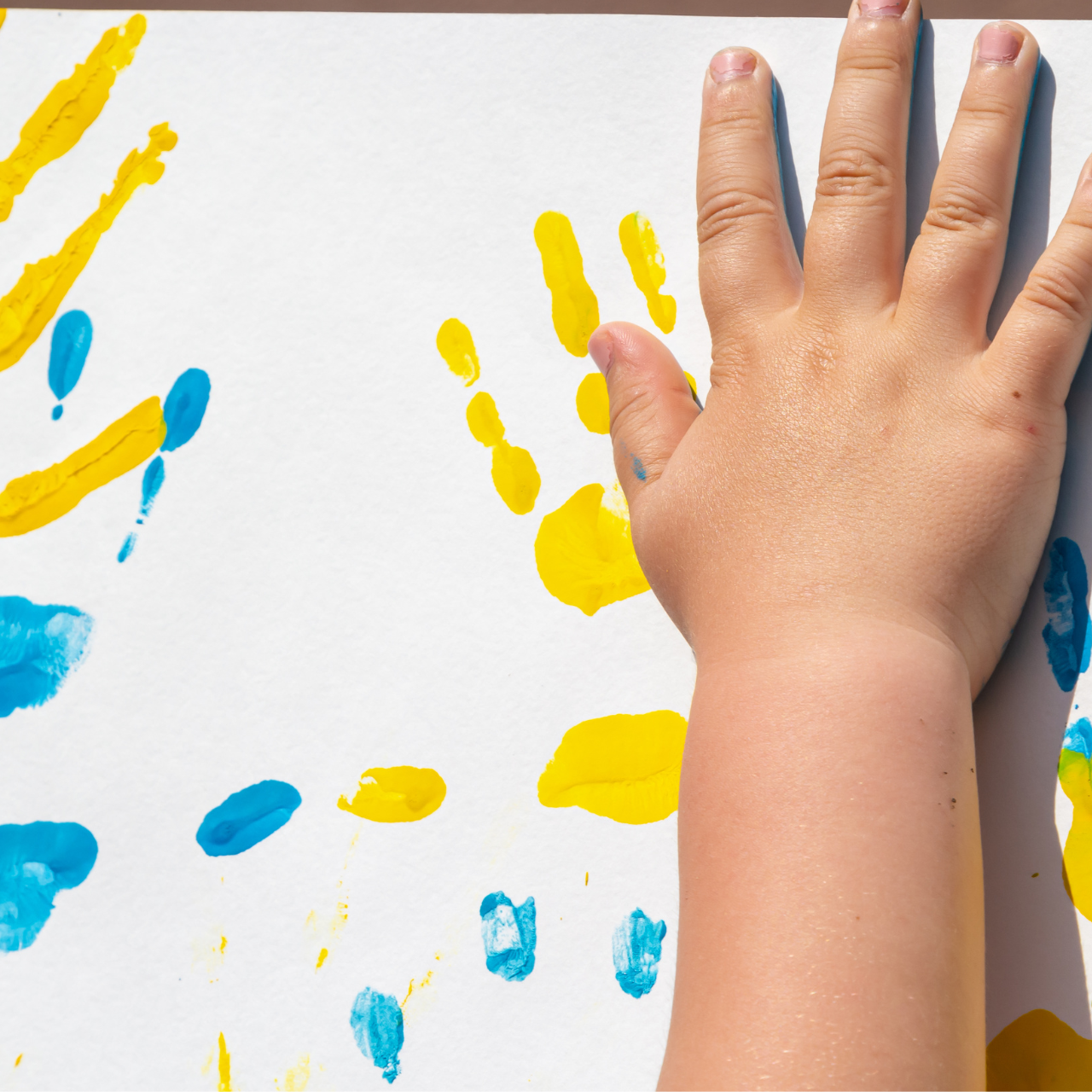 Criança fazendo carimbo de mão com tinta guache amarela e azul, brincadeira do 7 de Setembro