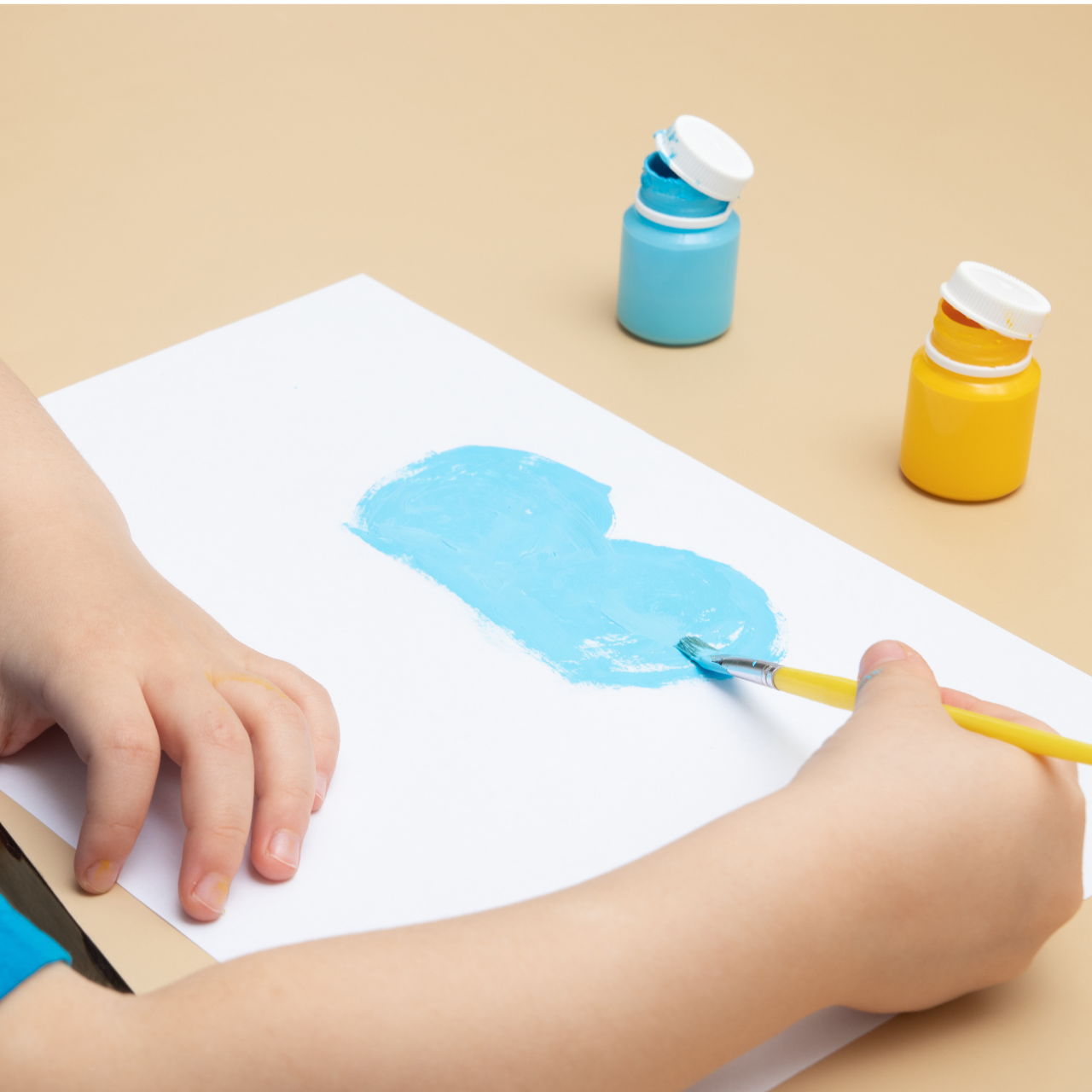 Criança pintando com pincel e tinta guache azul e amarela para brincadeira temática do 7 de Setembro