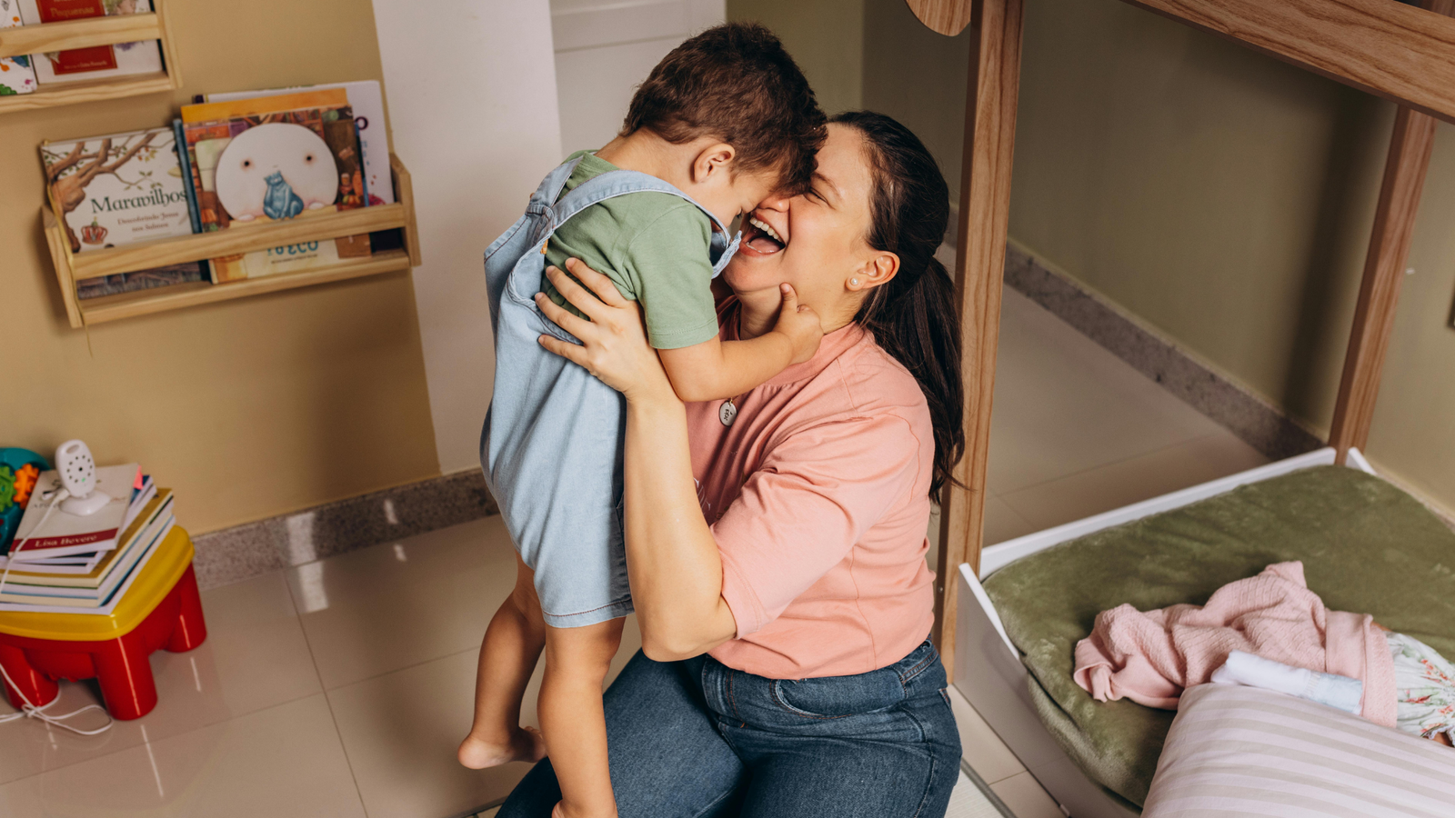 Mãe abraçando o filho pequeno em um quarto com estante de livros infantis