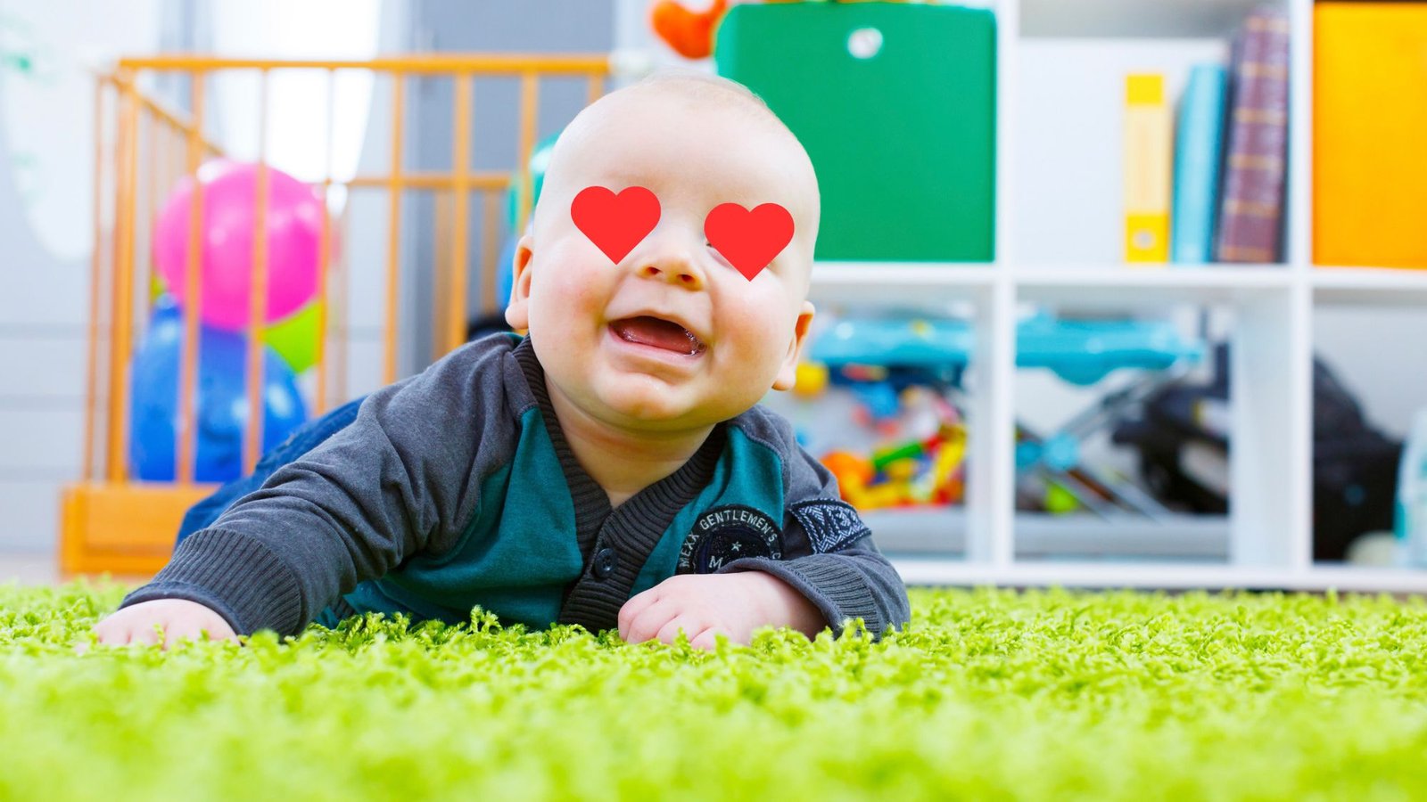 Bebê sorrindo, deitado de bruços em um tapete verde, em uma sala de brincar