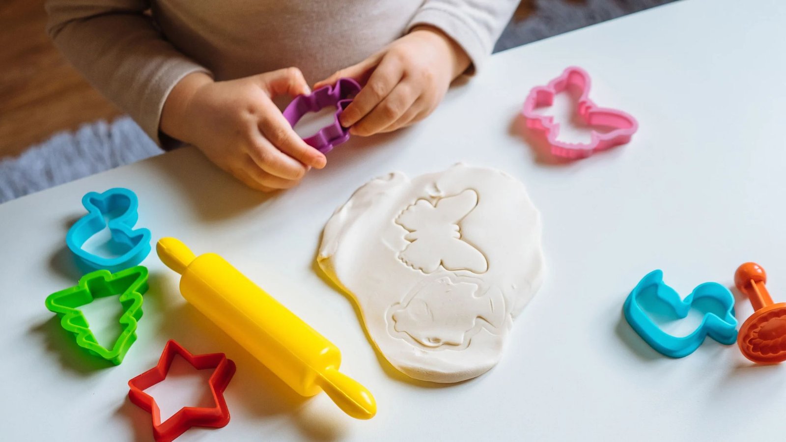 Criança brincando com massinha e formas coloridas sobre a mesa